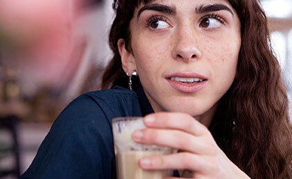 Frau schaut etwas skeptisch während sie einen Kaffee in der Hand hält